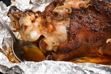 baked meat and fried onions on a baking sheet, pork ham on foil and wooden background, home cooking