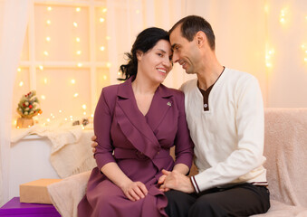 portrait of adult romantic couple sitting on a couch in home interior decorated with lights