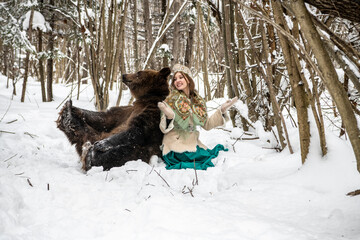 Russian beauty in folk national dress with a brown bear with a winter forest 