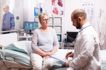 Obraz premium Senior woman listening doctor talking about treatment in examination room. Elderly patient having a converstation with medical stuff in private clinic during consultation.