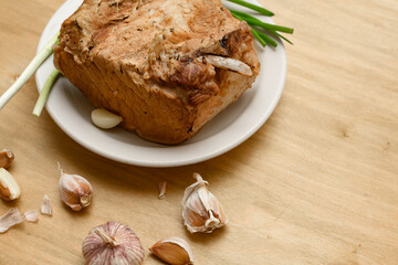 baked meat on a plate, green onion and garlic on wooden background, home cooking