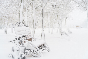 winter city park, benches covered in snow and snowfall