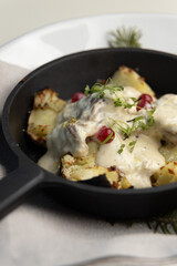 Fototapeta na wymiar Fried potatoes in a frying pan with cream gravy and berries close-up. Potatoes baked in coals with herbs, restaurant serving of the dish.