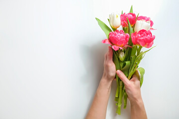 Cropped shot of woman's hands holding a bunch of tulips over white background. Female composing a bouquet. International Women's day greeting concept. Copy space, close up, top view, flat lay.