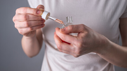 A woman is holding a bottle of fragrant natural oil and dropping a drop on the nail and cuticle. Concept of hand care and moisturizing the skin with oil. Closeup