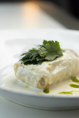 Scalding hot baked cabbage rolls with cream sauce close-up. Restaurant serving of cabbage rolls on a plate with greens.