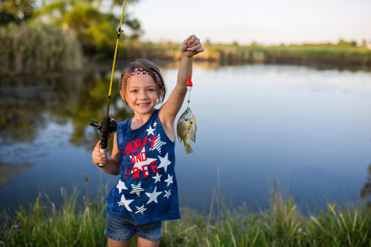 Portrait of girl showing off caught fish while standing against lake