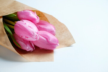 A bouquet of pink french single late tulips in craft paper wrapping. Tender minimalistic spring flowers composition isolated on white background. Close up, copy space, top view, flat lay, studio shot.