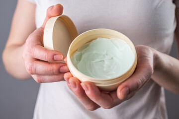 Woman in a white shirt is holding an open jar of cream. Concept of skin care and the use of natural cosmetics for face, body and hands. Closeup