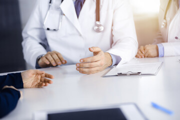 Patient woman and two doctors are discussing something while sitting at the desk in modern clinic. Perfect medical service, medicine concept