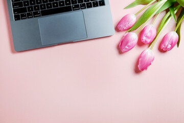 Fresh flower composition, bouquet of french tulips near the gray laptop with black keyboard, pale pink background. Office romance concept. Copy space, close up, top view, flat lay.