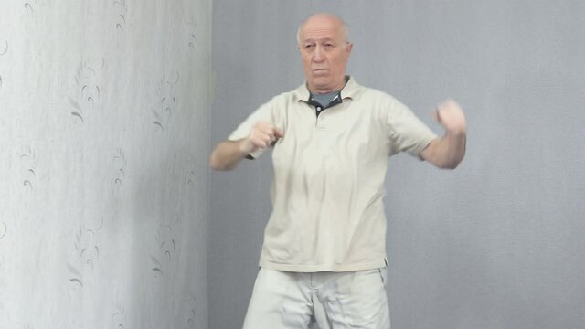 Old man in sportswear performs movements with arms and legs
