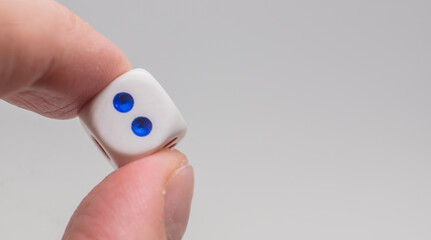 One dice with number two in hand. White dice on white background. Concept of luck, chance and leisure fun.
