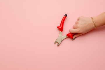 a woman's hand holds a pair of wire cutters. Wire cutters with electric protection in red on a pink background