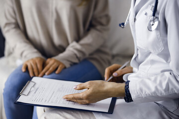 Unknown woman-doctor and patient discussing current health examination while sitting indoors. Stay...