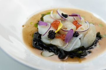 Sea salad with scallops and red caviar, on a white plate. Restaurant dish close-up, decorated with fresh flowers.