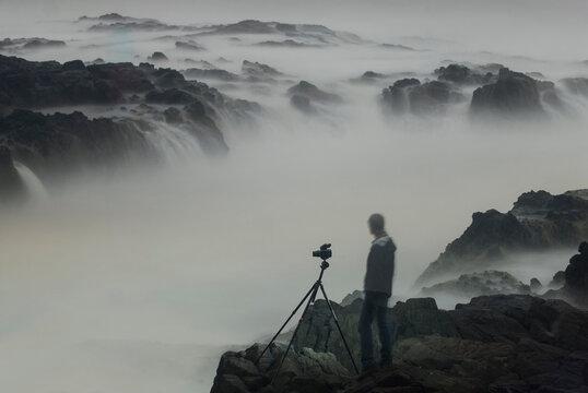 Digital composite image of hiker looking at Thor's Well while standing on rocks