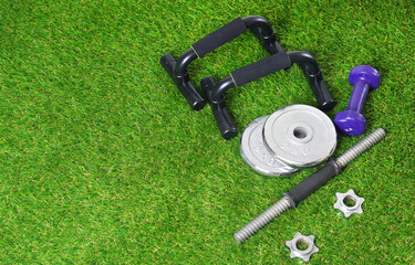 Fitness tools for physical training on the green artificial grass. Push up bars, dumbbells on the artificial turf. Copy space.