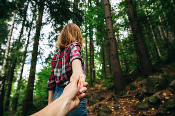 Naklejka premium Follow me photo in the mountains. Stylish woman in checkered shirt. Wanderlust concept. Couple hiking and travelling in summer. Holding hands in nature.