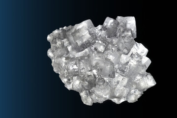 Aggregate of many almost transparent cubic salt crystals in front of a dark background