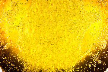 Liquid gold-yellow gasoline bubbles background on beer or champagne glass. Close up, macro shot.