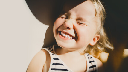 Cutest little girl smiling and squinting in sunlight. Happy toddler having fun. Portrait of playful...
