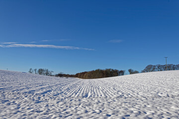 Fototapeta na wymiar A gentle V shaped Valley with a snow covered ploughed field with all the furrows covered in snow but still showing the definition of the furrows.