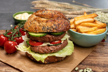 Tasty vegetarian vegan lunch with double decker hamburger made from plant based soya beans burger, organic bun with seeds and fresh vegetables and french fried potatoes