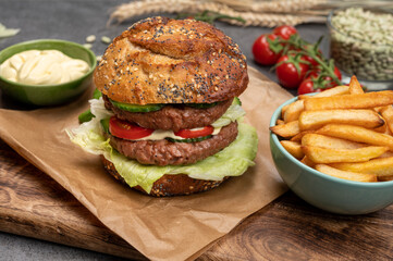 Tasty vegetarian vegan lunch with double decker hamburger made from plant based soya beans burger, organic bun with seeds and fresh vegetables and french fried potatoes