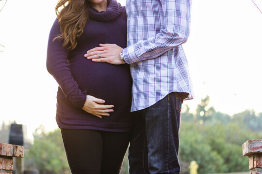 Midsection of husband touching pregnant wife's belly while standing against clear sky during sunset