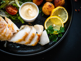 Fish dish - fried cod fillet with potatoes and vegetable salad on black wooden table
