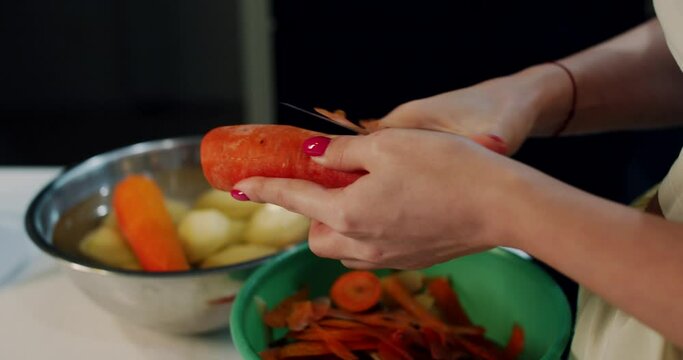 A carrot is cleaned with a woman's knife in the kitchen at home. Slow motion.