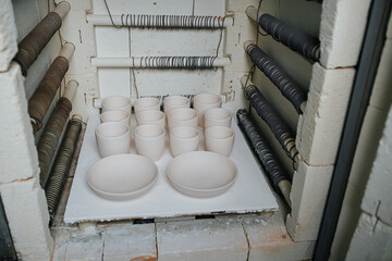 Fototapeta na wymiar Newly made blank tableware set up on a platform for firing in the kiln. Heating coils on the walls of the kiln.