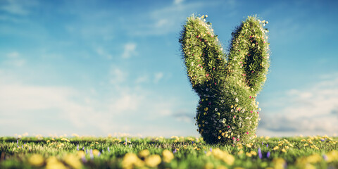 Easter bunny made of spring grass and flowers on green meadow.