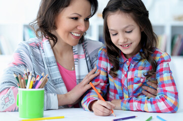 little cute girl with mother drawing at the table at home