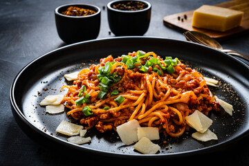 Spaghetti bolognese with minced pork meat and parmesan on black table
