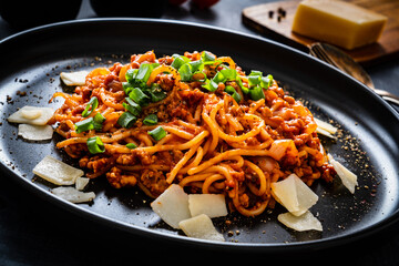 Spaghetti bolognese with minced pork meat and parmesan on black table