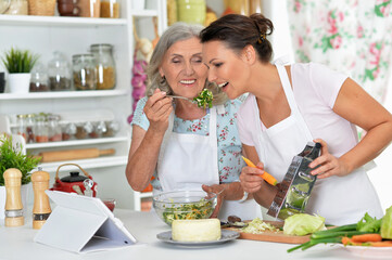 Smiling senior mother and adult daughter cooking together at kitchen