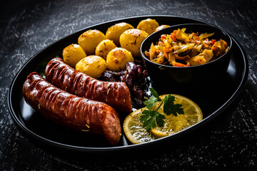 Fried sausages, fried potatoes, onion and fresh vegetables on black table