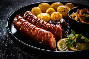 Fried sausages, fried potatoes, onion and fresh vegetables on black table