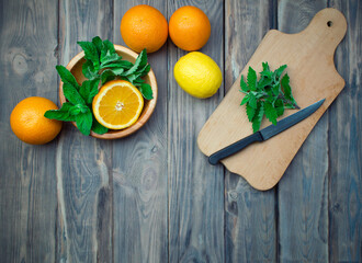 Citrus fruits and mint on a cutting board. Fresh summer citrus lemonade with lime, mint, oranges and ice cubes on shabby wood background. Making refreshing drinks.Kitchen summer background.