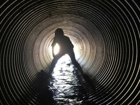 Rear view of silhouette boy standing in sewage tunnel
