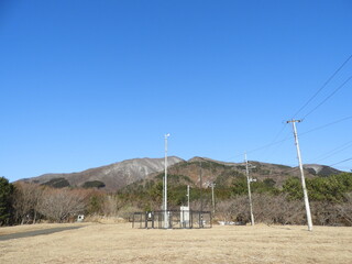 春を待つ里山と風向計