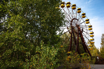 rusty abandoned ferris wheel in the autumn park with trees and sky