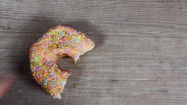 A delicious doughnut with colourful sprinkles having a bite taken out of it and put back down on a wooden work top