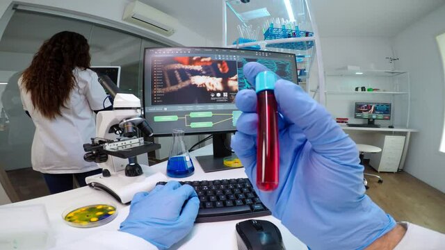 POV of virologist doctor holding tube with blood sampe typing information in pc, analysing patient disease, examining virus evolution. Team of scientists doing research working in equipped laboratory.