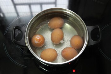 Boiled chicken eggs in a pot on an electric ceramic hob stove, top view.