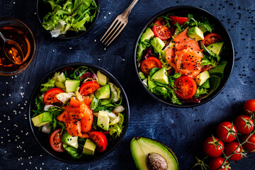 Salmon salad - smoked salmon with avocado and mix of vegetables on black wooden table
