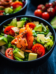 Salmon salad - smoked salmon with avocado and mix of vegetables on black wooden table
