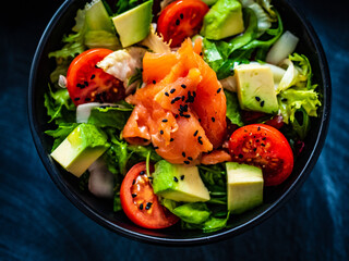 Salmon salad - smoked salmon with avocado and mix of vegetables on black wooden table
